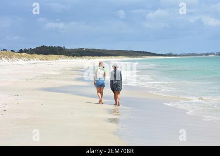 Zwei Weibchen am leeren weißen Sandstrand, gewaschen von milder Meeresbrandung. Stockfoto