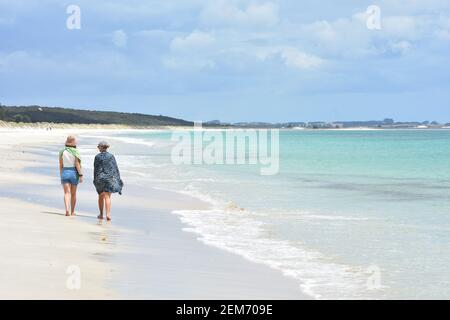 Zwei Frauen, die auf leerstem weißen Sandstrand laufen, der von milder Meeresbrandung gewaschen wird. Stockfoto