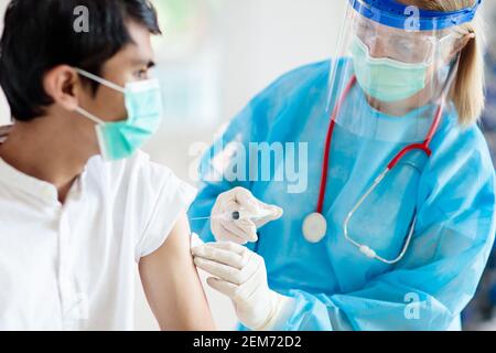 Injektion des Coronavirus-Impfstoffs in der Arztpraxis. Covid-19 Impfung im Krankenhaus. Arzt in Schutzanzug, der den Patienten untersucht. Krankenschwester mit Spritze. Asi Stockfoto