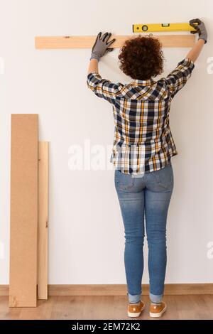 Unkenntlich Frau verwendet eine Ebene, um genau eine Holzdiele auf einer weißen Wand in einer Wohnung mit natürlichem Tageslicht zu platzieren. Stockfoto