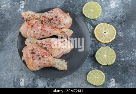 Rohe Hähnchenbeine mit Zitronenscheiben auf schwarzem Teller Stockfoto