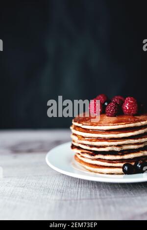 Saftige Pfannkuchen mit Beeren und Honig auf einem weißen Teller, Löffel, Holztisch. Hochwertige Fotos Stockfoto