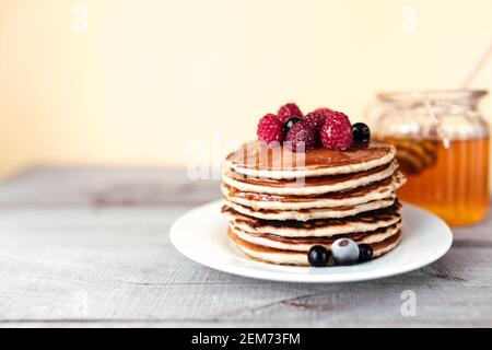 Saftige Pfannkuchen mit Beeren und Honig auf einem weißen Teller, Löffel, Glas, Holztisch. Hochwertige Fotos Stockfoto