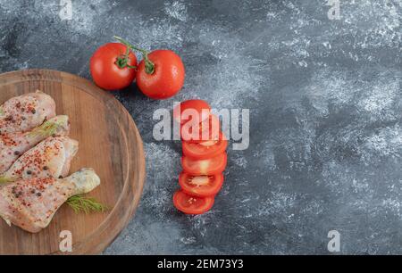 Rohe Hähnchenschenkel mit Gewürzen und geschnittenen oder ganzen Tomaten Auf einem Holzbrett Stockfoto