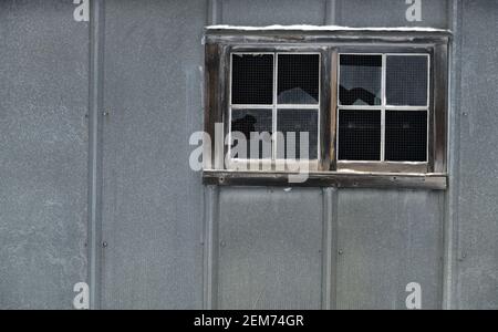 Kaputte Fenster mit etwas Schnee auf dem Fensterrahmen, in einem grauen, ländlichen Gebäude. Stockfoto