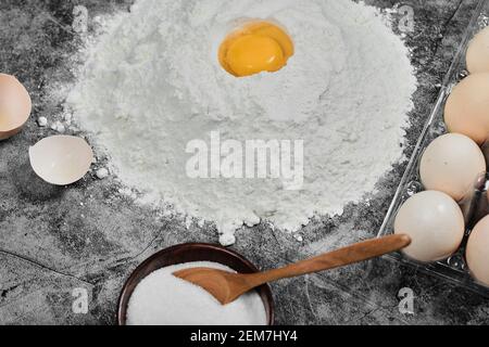 Eigelb auf Mehl, Eier, Schüssel Mehl und Whisker auf Stein Tisch Stockfoto