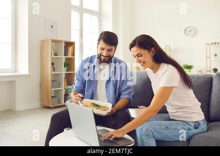 Mann und Frau schauen sich einen Film auf dem Laptop an und essen Essen zum Mitnehmen auf dem Sofa zu Hause. Stockfoto