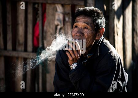 Chiang Mai / Thailand - Jan 16 2016 : der alte Asiate raucht und lächelt mit guter Laune, trägt alte Kleider, ein Bergstämmier in einem ländlichen Dorf in Nort Stockfoto