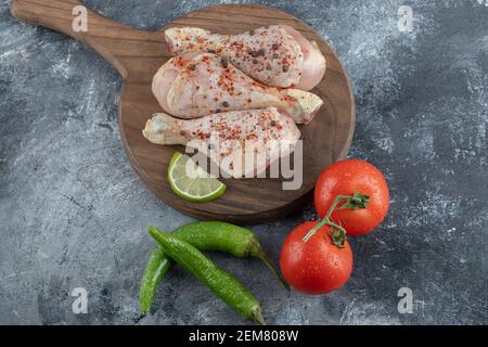 Rohe, würzige Hähnchenbeine auf einem Holzbrett mit Gemüse Stockfoto