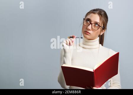 Nachdenkliches Mädchen macht Notizen in einem Notizbuch. Junge Studentin über isoliertem grauen Hintergrund. Stockfoto