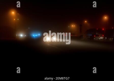 Autos im Dunst. Schlechtes Winterwetter und gefährlicher Autoverkehr auf der Straße. Leichte Fahrzeuge im Nebel. Stockfoto