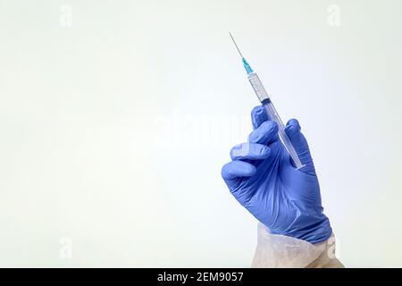 Hand trägt einen blauen Schutzhandschuh, der die Spritze isoliert hält Weiß Stockfoto
