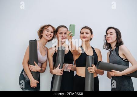 Lächelnde, freundliche Frauen, die sich im Yoga-Club unterhalten und Selfie machen Stockfoto