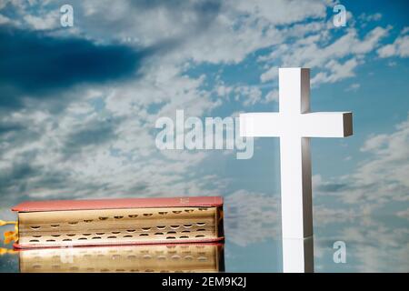 Helles weißes Kreuz neben einer heiligen bibel gegen den blau bewölkten Himmel. Stockfoto