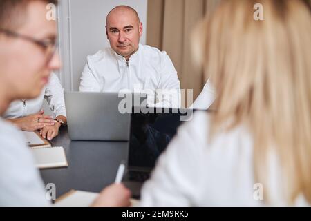 Der Chefarzt saß am Schreibtisch, umgeben von seinem Team Stockfoto