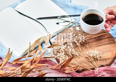 Tasse Tee mit Notizbuch, Gläsern und getrockneten Pflanzen auf weißem Schreibtisch halten Stockfoto