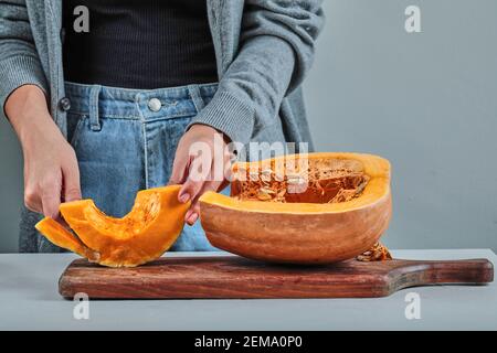 Eine Frau, die eine Scheibe Kürbis mit einem Messer schneidet Auf dem Holzbrett Stockfoto