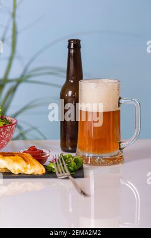 Appetitliches Bierglas umgeben von einer leeren Bierflasche und einem Schiefertablett mit gegrillten Käse-Sandwiches. Selektiver Fokus. Essen und Lifestyle-Konzept. Stockfoto