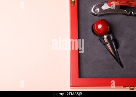 Geschenkset mit Korkenzieher und abnehmbaren Deckeln. Weinkorken und Flaschenöffner in einer Holzkiste auf rosa Hintergrund. Stockfoto