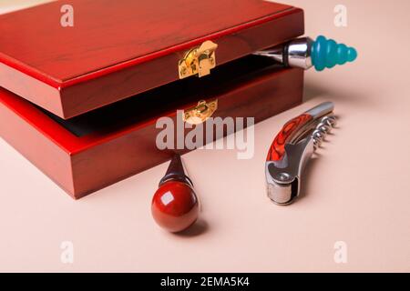 Geschenkset mit Korkenzieher und abnehmbaren Deckeln. Weinkorken und Flaschenöffner in einer Holzkiste auf rosa Hintergrund. Stockfoto