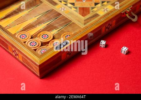 Ein unterhaltsames Backgammon-Spiel auf rotem Hintergrund. Steine, Würfel, handgemachtes Brett Stockfoto