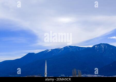 Herrlicher Berg (uludag) Blick vom Stadtzentrum mit Minarett einer Moschee und getrockneten Bäumen. Riesige Wolken und Schnee bleiben auf dem Berg. Stockfoto