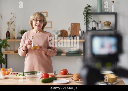 Ältere Frau in Brillen stehen am Küchentisch und Erzählen von Essen für die Kamera in der Küche Stockfoto