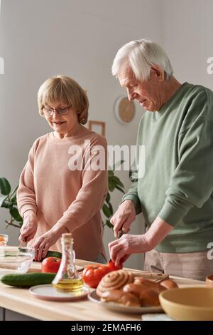 Seniorenpaar steht am Tisch und schneidet frisches Gemüse Für Gemüsesalat in der Küche Stockfoto