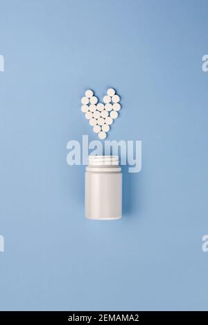 Blaue Pillen aus dem Glas in Form eines Herzens auf einem blauen Hintergrund gegossen, das Thema der Krankheiten. Stockfoto