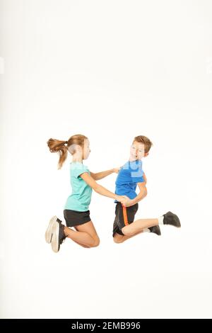 Fröhliche männliche Kind in Sportswear unter die Hände von entzückenden Mädchen beim Springen in die Luft. Isoliert auf weißem Hintergrund Stockfoto