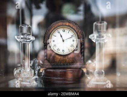 Alte mechanische hölzerne Aufwickeluhr, die im Antiquitätenladen steht Fenster mit Reflexionen auf Glas zu sagen Zeit elfte Minute 11:11 11th Uhr Stockfoto