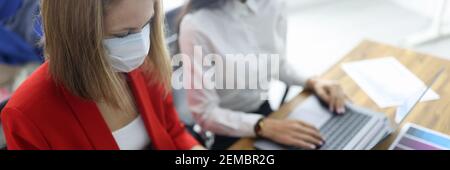 Zwei Frauen am Arbeitstisch in schützenden medizinischen Masken. Stockfoto