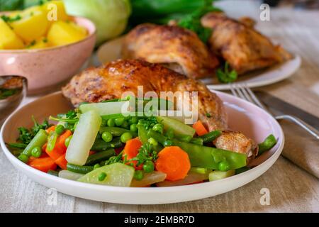 Gegrilltes Hähnchenschenkel mit Frühlingsgemüse auf einem Teller serviert Auf dem Esstisch Stockfoto
