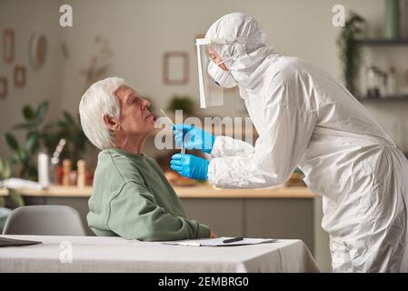 Älterer Mann, der den Coronavirus-Test mit einem Arzt in Schutzkleidung bestanden hat Eine Analyse zu Hause durchführen Stockfoto