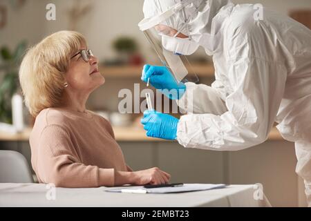 Ältere Frau sitzt im Krankenhaus und bestanden Coronavirus-Test mit Arzt in Schutzkleidung nimmt eine Probe für die medizinische Untersuchung Stockfoto