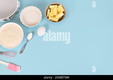 Zutaten zum Backen von Teig für Mürbeteig mit Mehl, Zucker, Backpulver und Ei in Schüsseln auf blauem Hintergrund mit leerem Kopierraum Stockfoto