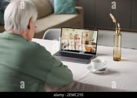 Rückansicht des älteren Mannes, der am Tisch sitzt und Mit dem Laptop online mit seinem Freund zu Hause zu sprechen Stockfoto