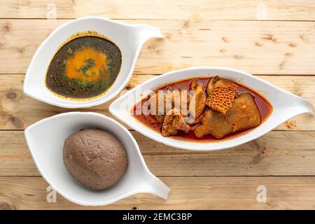 Amala mit Ewedu und gemischtem Fleisch in Eintopf in Keramik Schüsseln auf einer Holzfläche von oben Stockfoto