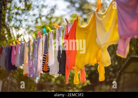 Baby niedliche Kleidung hängen auf der Wäscheleine im Freien. Kinder Wäsche hängt auf Linie im Garten auf grünem Hintergrund.Baby Zubehör. Stockfoto