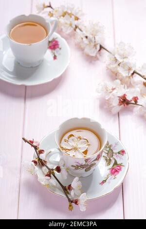 Zweige blühender Aprikosen und zwei Porzellanbecher mit Tee und auf hellrosa Holztisch. Stockfoto