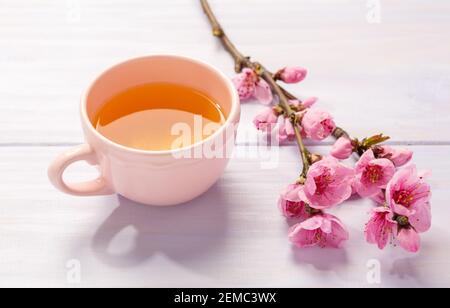 Tasse Tee und Zweige der blühenden Pfirsich auf Holztisch. Stockfoto