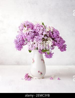 Blumenstrauß von Flieder in alter Porzellanvase auf einem weißen Holztisch. Selektiver Fokus. Stockfoto