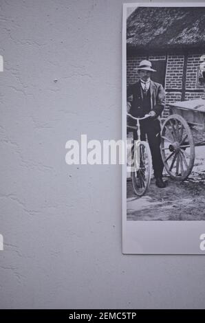 Direkt oberhalb von 1910 ländliches Schwarz-Weiß-Foto des Mannes im Hut mit Fahrrad neben dem Wagen. Konzept, ländliche Leben, 1900 Lebensstil, Transport Stockfoto