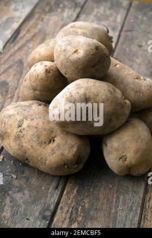 Haufen Kartoffeln auf hölzernen Brettern mit einem Kartoffelbeutel Im Hintergrund Stockfoto