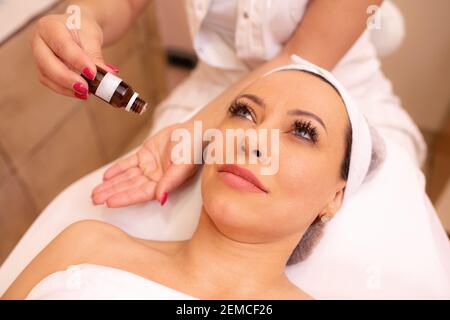 Masseuse Anwendung von Massageöl auf ihre Hände vor Beginn einer Gesichtsmassage auf eine Frau mittleren Alters, Gesichtsmassage Konzept Stockfoto