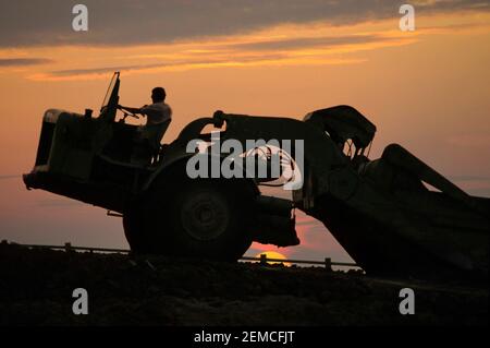 Siehe Alamy Image Ref WR6G0B, um die Art der Landschaft zu sehen, in der diese Maschine arbeitete. Historisches Archiv der 1970er Jahre Nahaufnahme eines männlichen Fahrers und einer Maschine in Silhouette, die spät mit dem Sonnenuntergang am Himmel arbeitete, über das Fahren eines großen Motorkratzers, Erde, schwere Pflanze, die eine von vielen Kratzern und den Transport von Erde zu Dämmen für tiefe Schnitte bewegte, ein Archivbild der großen Tiefbauinfrastruktur der 70er Jahre Bauvorhaben auf der neuen umkreisförmig umlaufgelegenen Londoner Autobahnstraße M25 im Jahr 1977 in Brentwood Essex England, Großbritannien, in der Nähe der Anschlussstelle 28 Stockfoto