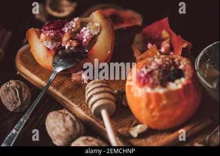 Gebackene Äpfel mit Hüttenkäse mit Beeren und Nüssen, mit Honig gekrönt und mit Zimt bestreut. Auf einer hölzernen Oberfläche in einem rustikalen Stil Stockfoto