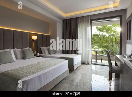 Modernes Apartment-Interieur des Familienhotels mit grauen Eichenholzmöbeln, Einzel-, Doppel-King-Size-Bett. Modernes Schlafzimmer mit offenem großen Fenster, Stockfoto