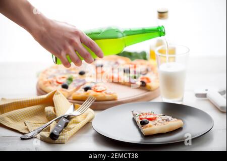 Frische Pizza im rustikalen italienischen Stil mit ruckigen Oliven Die Pilze und drei Arten des Käses auf dem hellen hölzernen Hintergrund mit einer Flasche kaltes Bier Stockfoto