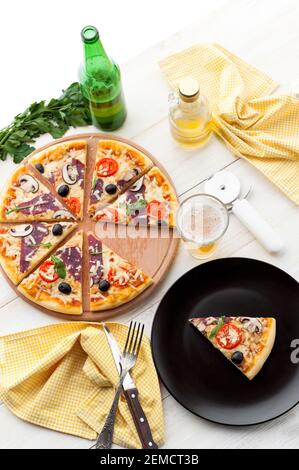 Frische Pizza im rustikalen italienischen Stil mit ruckigen Oliven Die Pilze und drei Arten des Käses auf dem hellen hölzernen Hintergrund mit einer Flasche kaltes Bier Stockfoto